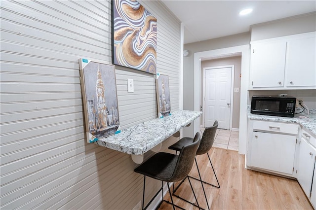 kitchen with light stone countertops, light hardwood / wood-style floors, a kitchen bar, and white cabinetry