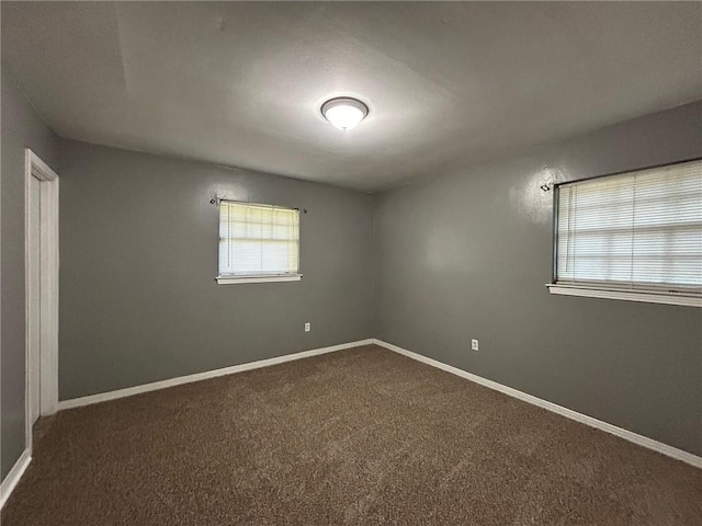 empty room featuring dark colored carpet and baseboards