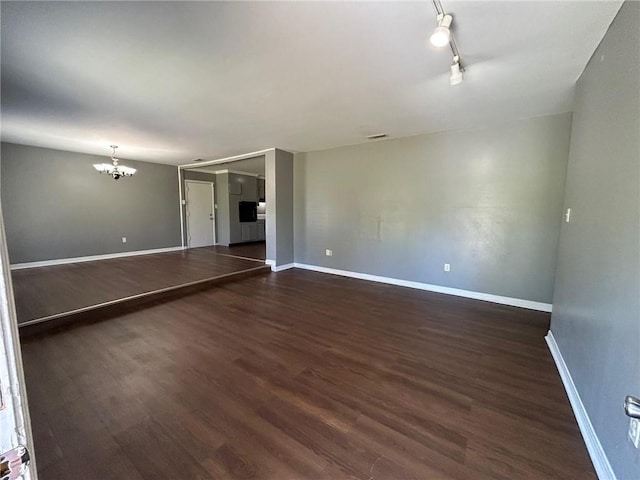 spare room with an inviting chandelier, rail lighting, baseboards, and dark wood-style floors