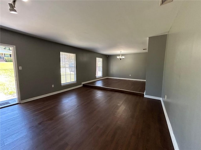 spare room with visible vents, baseboards, dark wood-style floors, and a notable chandelier