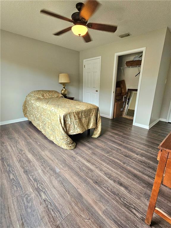 bedroom featuring ceiling fan, a textured ceiling, a closet, dark hardwood / wood-style floors, and a spacious closet