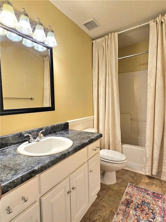 full bathroom with vanity, toilet, a textured ceiling, and shower / tub combo with curtain