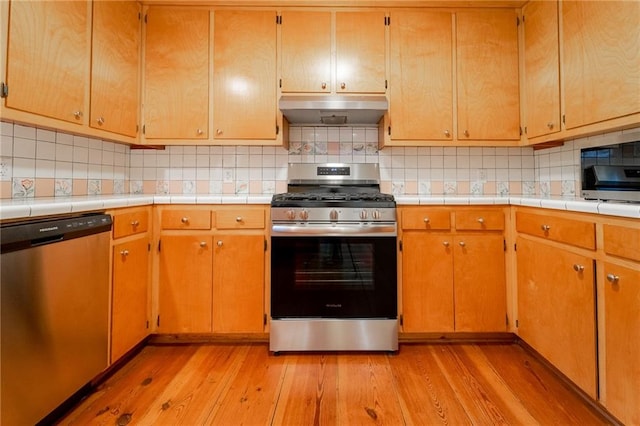 kitchen featuring stainless steel appliances, tile counters, tasteful backsplash, and light hardwood / wood-style floors