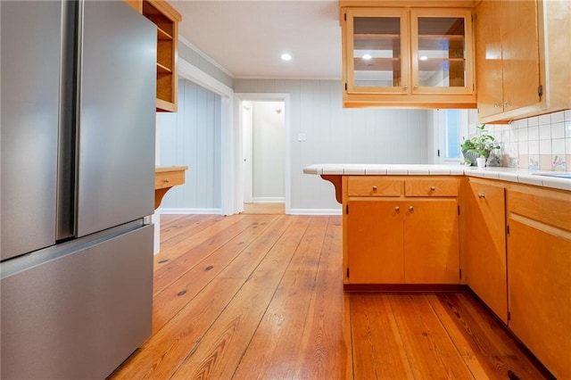 kitchen with tile counters, stainless steel fridge, light wood-type flooring, and wooden walls