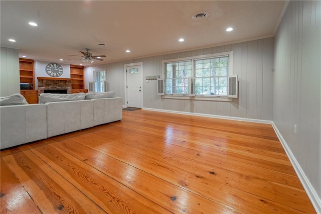 unfurnished living room featuring ceiling fan, wood walls, crown molding, and light hardwood / wood-style flooring