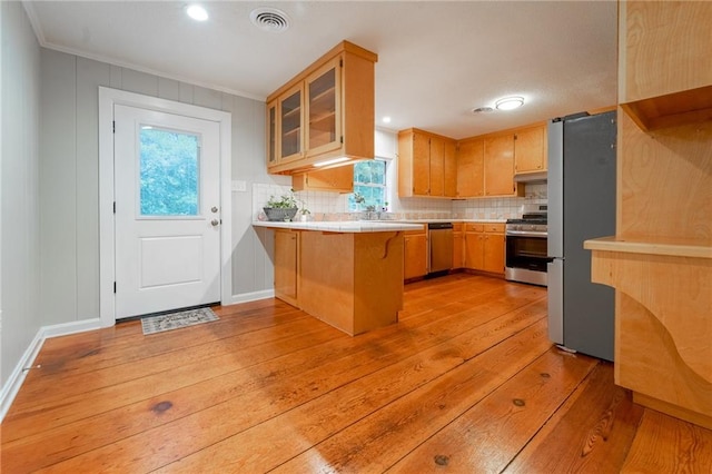 kitchen with kitchen peninsula, decorative backsplash, light wood-type flooring, a kitchen bar, and stainless steel appliances