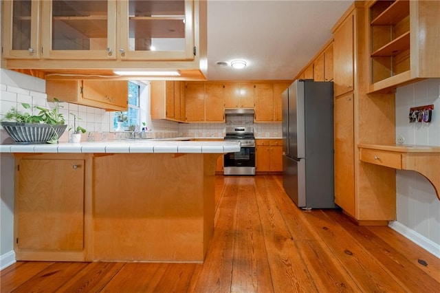 kitchen featuring backsplash, tile countertops, kitchen peninsula, light hardwood / wood-style floors, and appliances with stainless steel finishes