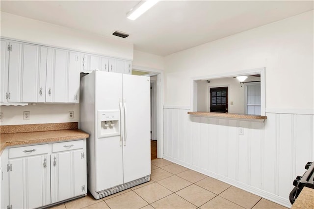 kitchen featuring white refrigerator with ice dispenser, light tile patterned floors, and white cabinets