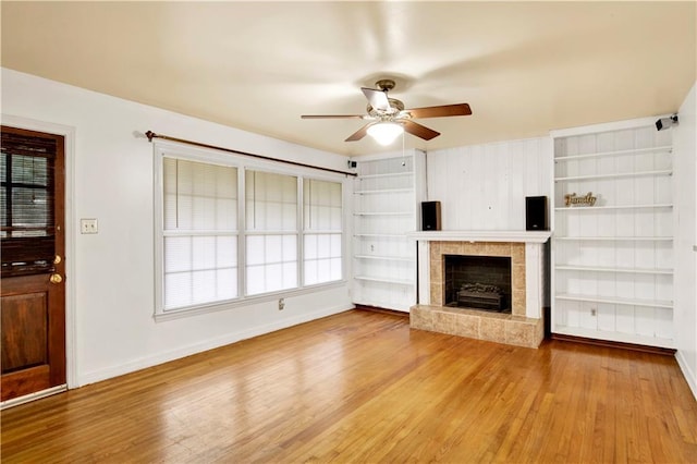 unfurnished living room featuring ceiling fan, wood-type flooring, a fireplace, and built in features