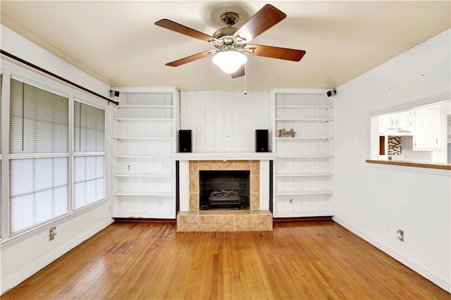 unfurnished living room featuring hardwood / wood-style floors, built in shelves, a tile fireplace, and ceiling fan