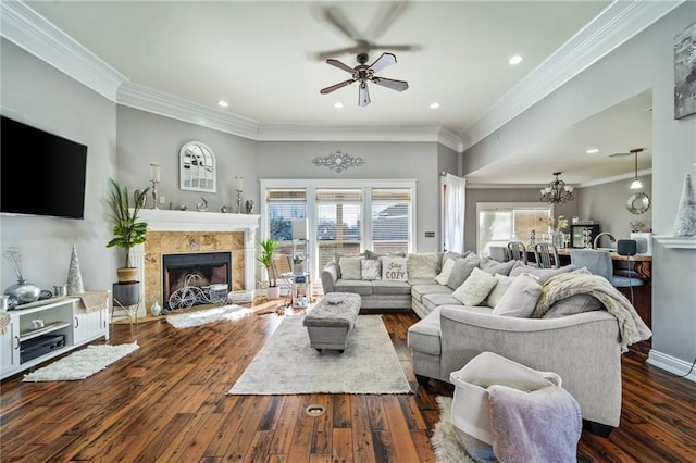 living room featuring a tiled fireplace, ceiling fan with notable chandelier, ornamental molding, and dark hardwood / wood-style floors