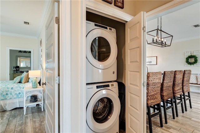 laundry area featuring stacked washer / drying machine, crown molding, and light hardwood / wood-style flooring