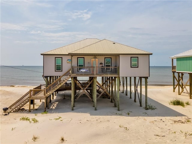 rear view of property with a carport, a water view, a beach view, and covered porch