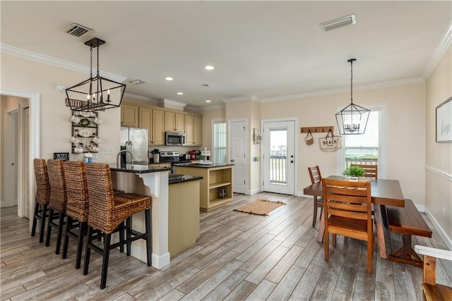 kitchen featuring a kitchen bar, decorative light fixtures, light wood-type flooring, ornamental molding, and stainless steel appliances