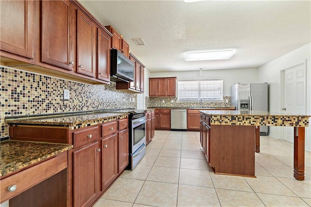 kitchen with a center island, backsplash, dark stone countertops, light tile patterned floors, and appliances with stainless steel finishes