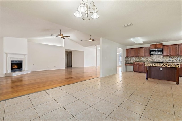 kitchen featuring decorative backsplash, pendant lighting, a fireplace, light hardwood / wood-style floors, and lofted ceiling