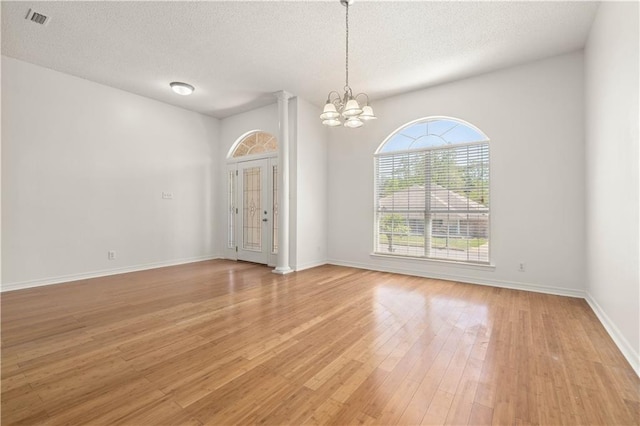 empty room with a chandelier, a textured ceiling, and light hardwood / wood-style floors