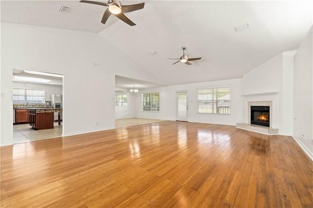 unfurnished living room featuring ceiling fan with notable chandelier, light hardwood / wood-style floors, and high vaulted ceiling