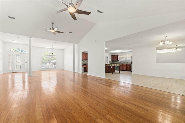 unfurnished living room with ceiling fan with notable chandelier, vaulted ceiling, and light hardwood / wood-style flooring