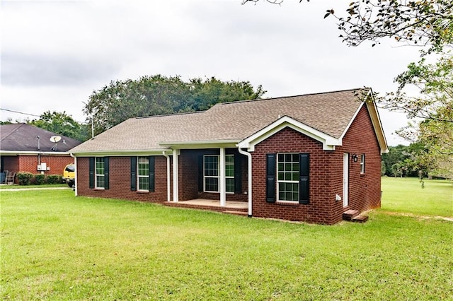 rear view of property with brick siding, a patio area, a lawn, and roof with shingles