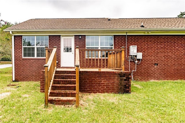 back of property featuring brick siding, a lawn, and roof with shingles