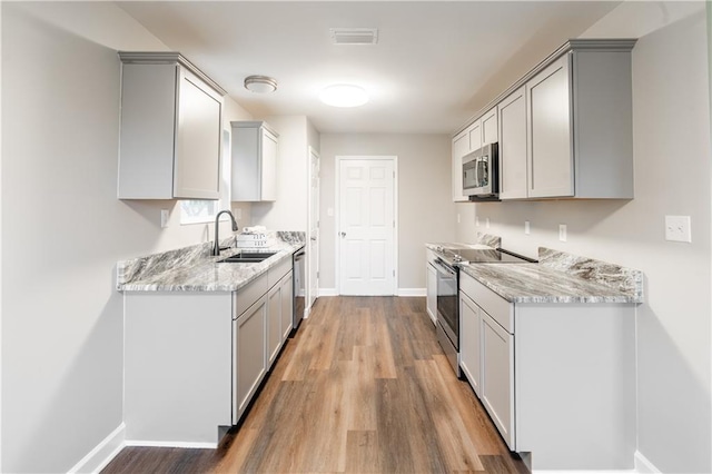 kitchen with wood finished floors, baseboards, gray cabinets, a sink, and stainless steel appliances