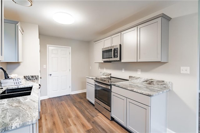 kitchen with light stone counters, light wood finished floors, gray cabinets, a sink, and appliances with stainless steel finishes