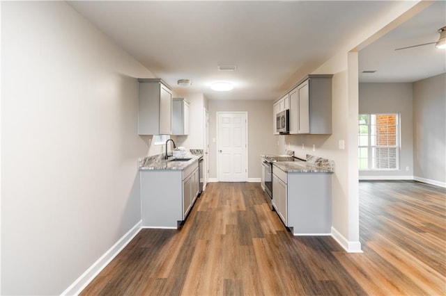 kitchen with baseboards, gray cabinets, dark wood-style flooring, a sink, and stainless steel appliances