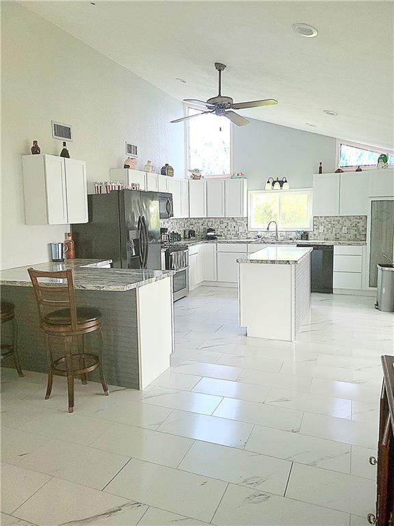 kitchen featuring white cabinets, a center island, marble finish floor, light countertops, and black appliances