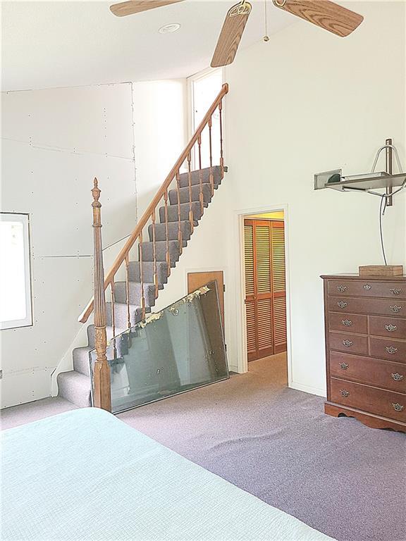 bedroom featuring light carpet, a high ceiling, and a ceiling fan