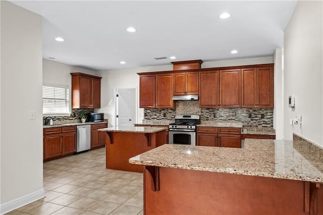 kitchen with dishwasher, light stone counters, stainless steel gas range, under cabinet range hood, and a kitchen bar