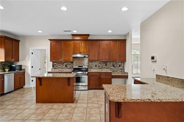 kitchen featuring stainless steel appliances, backsplash, light stone countertops, under cabinet range hood, and a kitchen bar