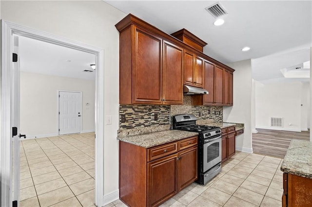 kitchen with under cabinet range hood, stainless steel gas range oven, light tile patterned floors, and visible vents