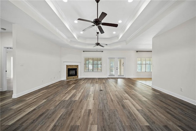 unfurnished living room featuring a tray ceiling, dark wood-style flooring, crown molding, a high end fireplace, and baseboards