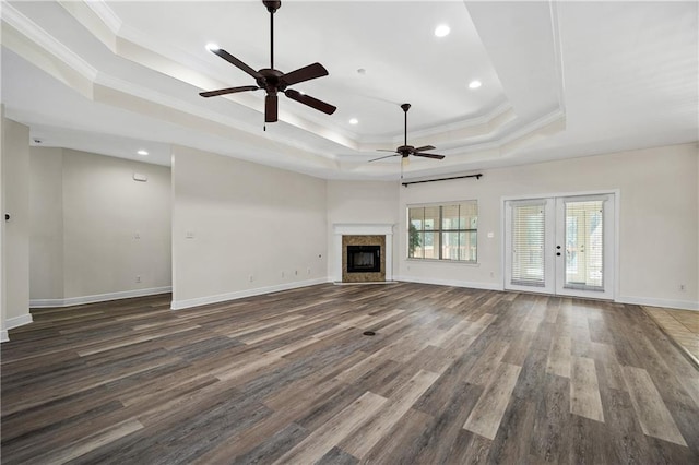 unfurnished living room with a fireplace, wood finished floors, baseboards, ornamental molding, and a tray ceiling