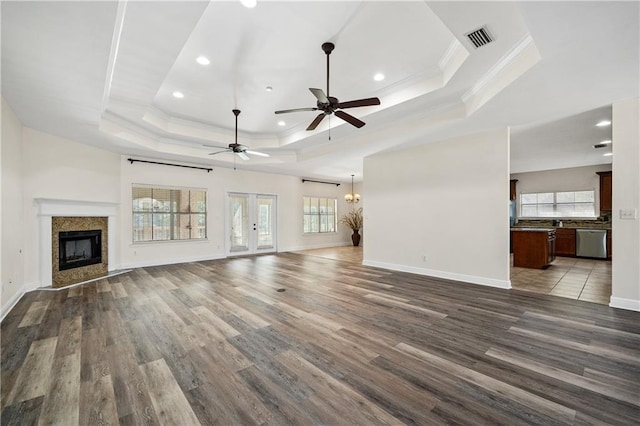 unfurnished living room featuring crown molding, a fireplace, a raised ceiling, visible vents, and wood finished floors