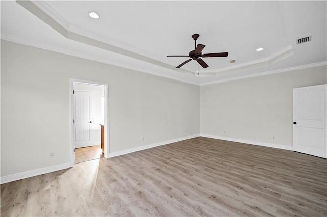 spare room featuring crown molding, a raised ceiling, visible vents, light wood-style flooring, and baseboards