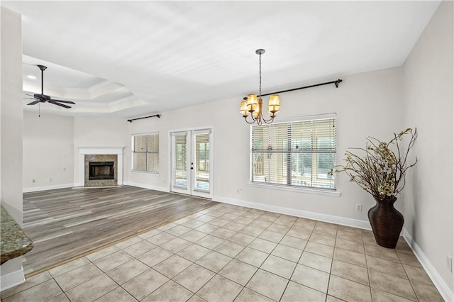 unfurnished living room with a tray ceiling, crown molding, a high end fireplace, baseboards, and ceiling fan with notable chandelier