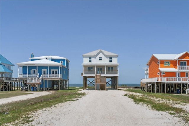 raised beach house with a carport, dirt driveway, a water view, and stairs