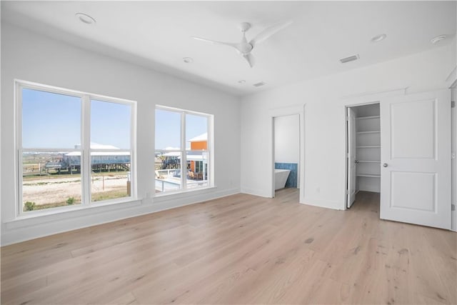 unfurnished bedroom featuring multiple windows, baseboards, light wood-style floors, a walk in closet, and recessed lighting