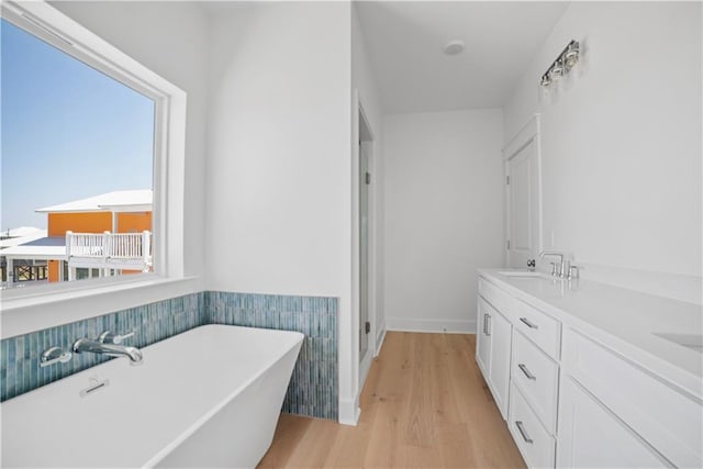 full bath featuring a sink, a soaking tub, wood finished floors, and baseboards