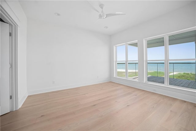 spare room featuring a water view, light wood-type flooring, baseboards, and a ceiling fan