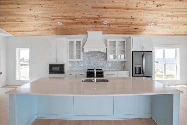 kitchen featuring custom exhaust hood, black appliances, wood ceiling, a sink, and a large island with sink