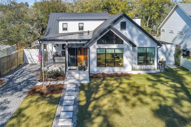 modern farmhouse style home featuring a chimney, covered porch, a front yard, a standing seam roof, and fence