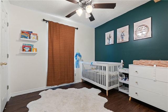 bedroom featuring ceiling fan, dark wood-type flooring, and a nursery area