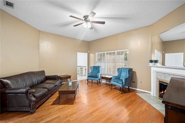 living area with visible vents, ceiling fan, a tile fireplace, wood finished floors, and a textured ceiling