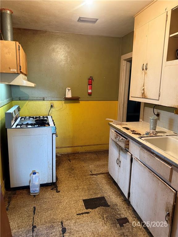 557 Kent St, Mobile, AL 36617 - kitchen with white gas range, under cabinet range hood, light countertops, baseboards, and a sink