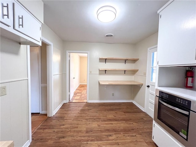 kitchen with white cabinetry, oven, and hardwood / wood-style floors