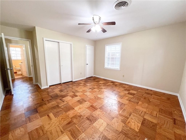 unfurnished bedroom with multiple closets, ceiling fan, light parquet flooring, and ensuite bathroom