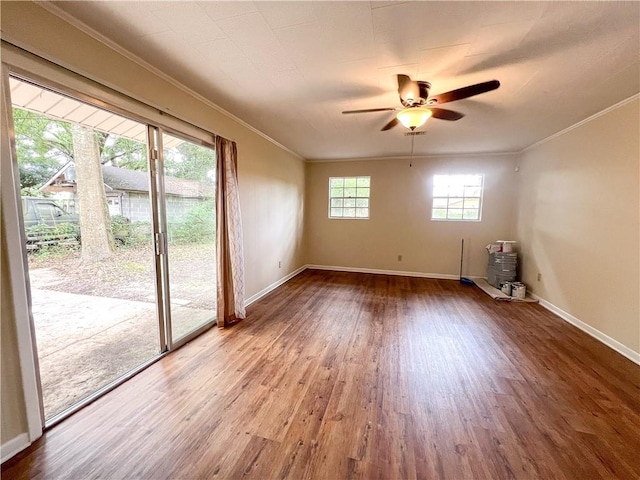 spare room with wood-type flooring, ornamental molding, ceiling fan, and a wood stove